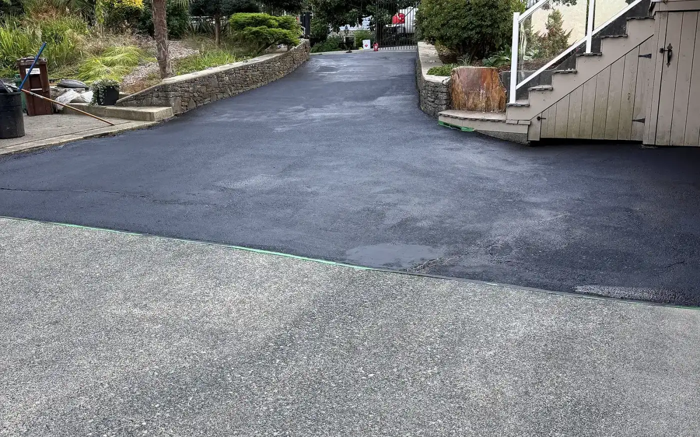 Asphalt driveway after sealcoating, deep uniform finish beside the wooden stairs