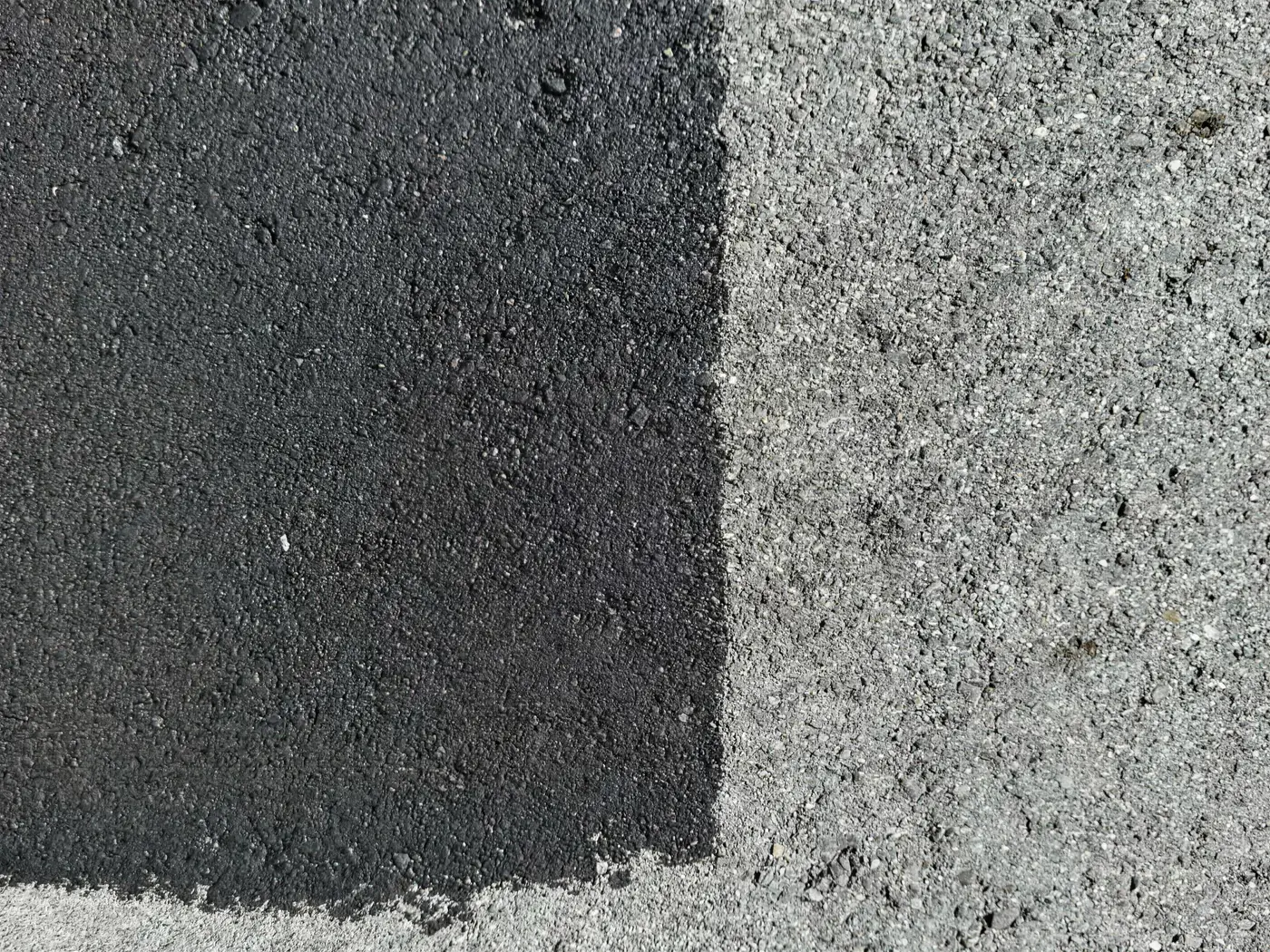 Close-up of freshly sealed asphalt meeting untreated pavement